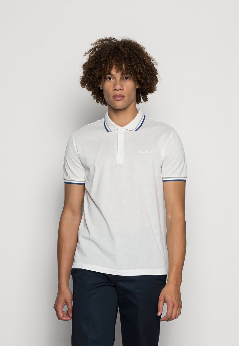 Camisa polo branca com uma textura suave, apresentando uma pala de três botões e riscas em azul-marinho contrastantes no colarinho e nas mangas.