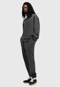 Mørkegrå sweatshirt og matchende træningsbukser lavet af blødt stof, med tone-i-tone logo detaljer. Sorte sneakers med hvide snørebånd og gummisåler.