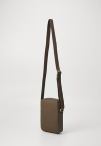 Geantă crossbody maro, cu formă rectangulară, exterior texturat și curea împletită. Dispune de o închidere cu fermoar și un design minimalist.