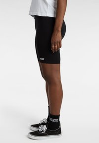 Pantalones cortos de ciclismo negros de tejido elástico, con el logo de Vans. Combinados con zapatillas negras de Vans y calcetines de longitud media con el logo.