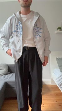 Light gray zip-up hoodie with blue sun graphics on the chest, worn over a white t-shirt, paired with black wide-leg pants and a black belt.