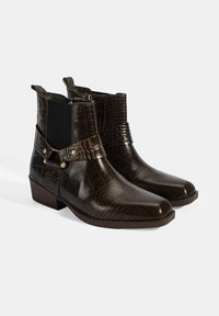 Bottines cheville à motif crocodile brun, avec un talon bloc, des panneaux latéraux élastiques et une sangle décorative avec des accents dorés.