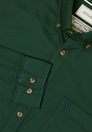 Dark green long-sleeve shirt with brown buttons, buttoned cuffs, embroidered logo on pocket, and a visible inside label.