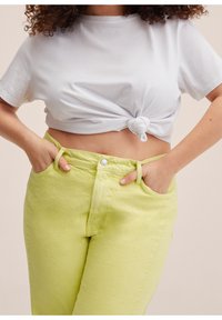 Camiseta blanca corta con un nudo en la parte delantera, combinada con unos pantalones vaqueros de mezclilla verde lima claros de tiro alto que cuentan con bolsillos delanteros y trabillas para cinturón.