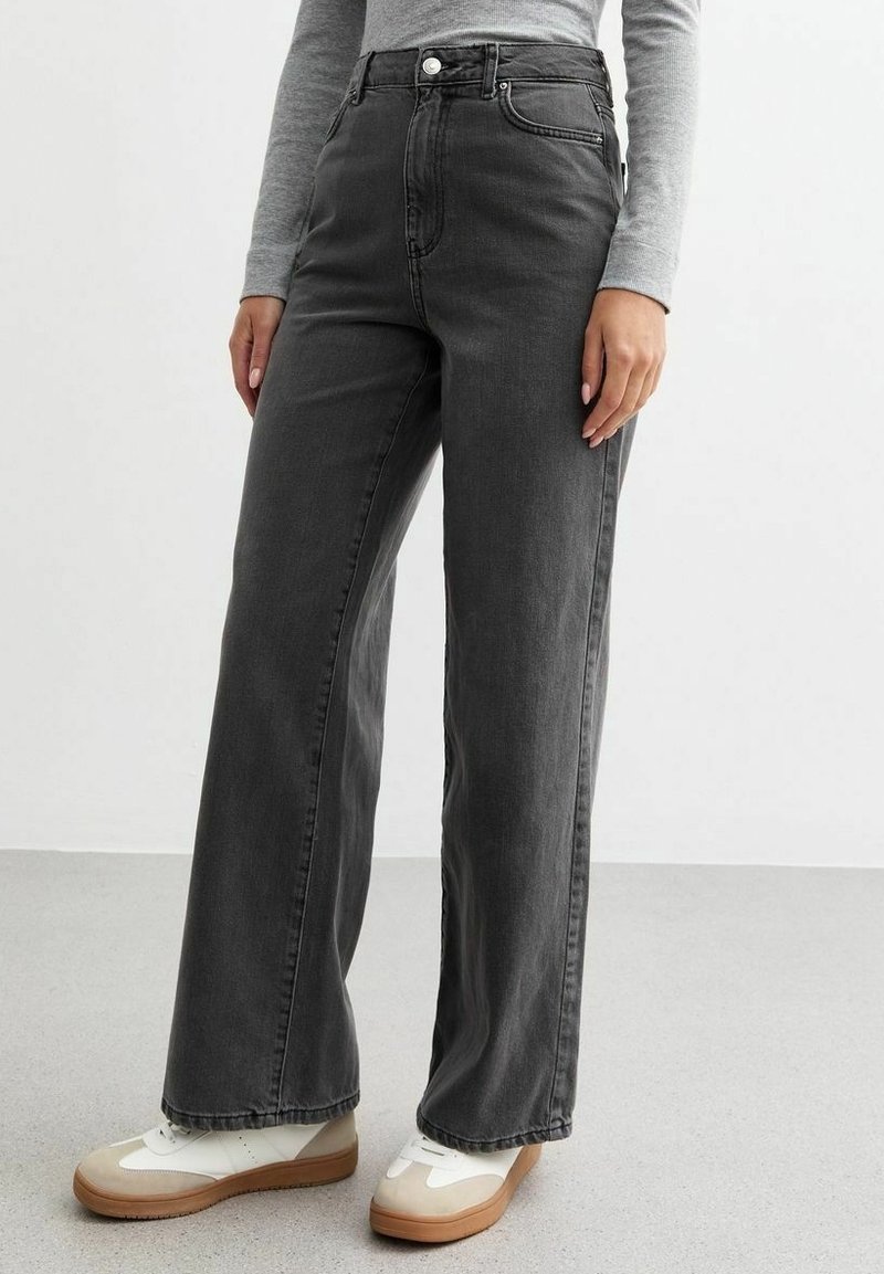 Korkeavyötäröiset, leveälahkeiset farkut tummanharmaasta denimistä. Ominaisuuksia ovat napin ja vetskarin sulkeminen, etutaskut ja sileä pinta. Yhdistetty valkoisiin lenkkikengiin.