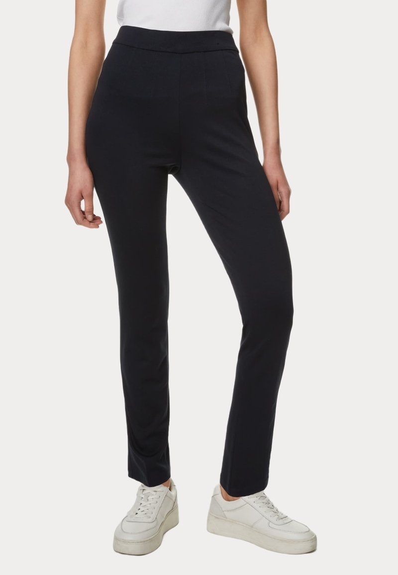 Námořnické kalhoty na míru s hladkou texturou, slim fit a vysokým pasem. Mají přední kapsy a jsou kombinovány s bílými teniskami.