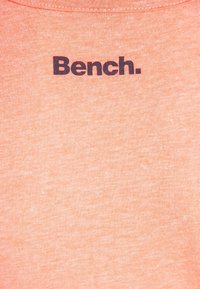 Brzoskwiniowy, bawełniany t-shirt z okrągłym dekoltem i czarnym napisem "Bench." z przodu. Miękka tekstura o gładkim wykończeniu.