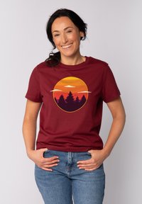 T-shirt en coton bordeaux avec un graphisme de coucher de soleil rond en orange et violet, avec des arbres silhouettés en dessous, à manches courtes et coupe classique.