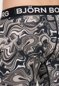 Leggingi u boji crne, sive i bijele mramorirane uzorke s vidljivim šavovima; crni elastični pojas s natpisom "BJÖRN BORG". Glatka tekstura tkanine.