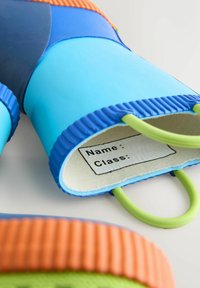 Bunte Gummitasche mit blauen, orangefarbenen und grünen Akzenten. Besitzt eine gerippte Textur und grüne Griffe. Enthält ein weißes Etikett für Namen und Klassen.