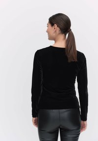 Svart sammetsblus med långa ärmar, rund halsringning, skräddarsydd passform och mjuk textur. Bärs tillsammans med svarta figurnära byxor.