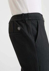 Zwarte broek van een gestructureerde stof, met een elastische tailleband en een achterzak met een rond merkembleem.