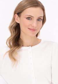 Bílý svetr s kulatým výstřihem, který má malé knoflíky ve tvaru perel podél přední části a měkkou pletenou texturu.