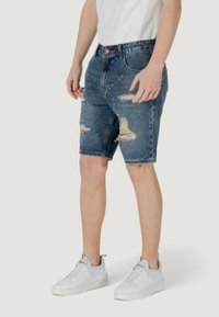 Shorts in denim con lavaggio blu, con dettagli scoloriti e orlo sfilacciato. Abbinati a sneakers bianche per un look informale.