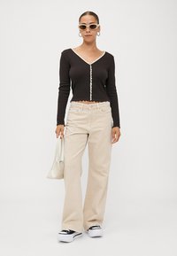 Black fitted long-sleeve top with scalloped hem, button detail, beige wide-leg pants, black and white sneakers, and a small white handbag.