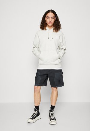 Lys grå hættejakke med snoretræk, frontlomme og broderet logo, parret med mørke cargo shorts og sorte høj-top sneakers.
