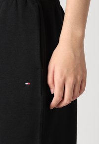 Zwarte katoenen joggers met een elastische tailleband, zijzakken en een klein geborduurd logo in rood, wit en blauw nabij de zak.