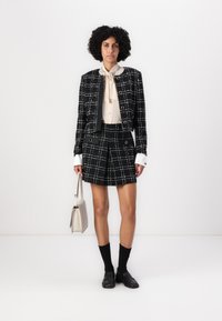 Black and white checkered suit with a cropped jacket and matching shorts, paired with a cream blouse, black socks, and loafers. Includes a beige handbag.