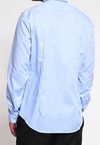 Ljusblå långärmad skjorta med rundad nederkant, knappdetaljer vid ärmarna och en mjuk textur. Lämplig för både avslappnad och formell klädsel.