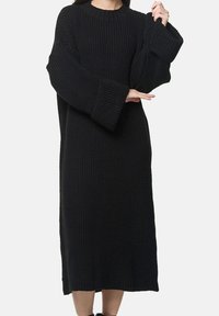 Czarna dzianinowa sukienka z oversize'owymi rękawami, prążkowaną fakturą, długością do połowy łydki i okrągłym dekoltem. Bez widocznych zapięć ani wzorów.