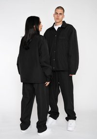 Jachete negre supradimensionate cu pantaloni asortați, având o croială lejeră și un design minimalist. Adidașii albi completează aspectul monocrom.