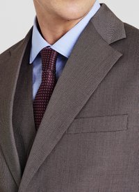 Braun kariertes Sakko mit Revers, kombiniert mit einem hellblauen Hemd und einer dunkelroten Krawatte, die mit kleinen weißen Punkten gemustert ist. Dünner, strukturiertes Gewebe.