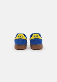 Sinised sametist tossud kollaste aktsentidega, kummitald ja tugevdatud kand. Brändinimi "NIKE" on näha kandel.