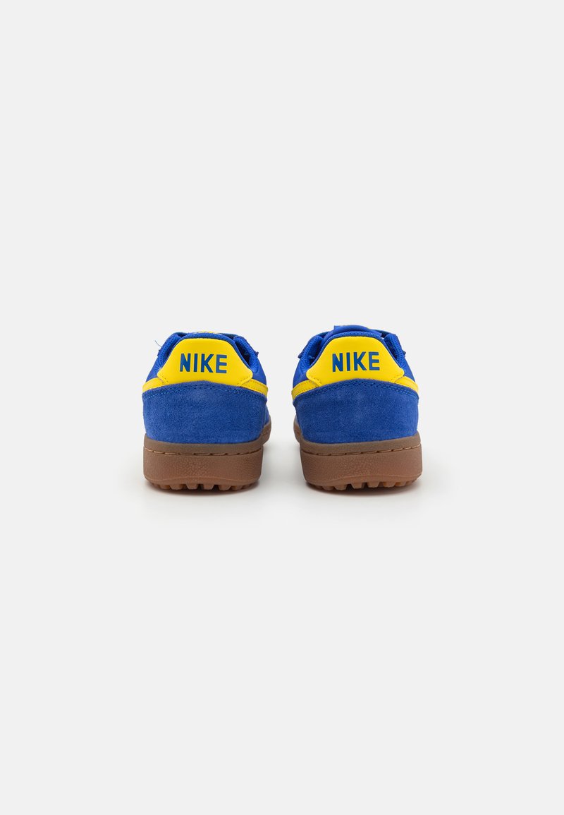Zapatillas de ante azul con acentos amarillos, que cuentan con una suela de goma y un talón reforzado. Nombre de la marca "NIKE" exhibido en el talón.