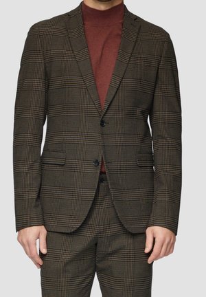 Homme portant un costume à carreaux marron et noir avec une veste à deux boutons et un pantalon assorti, associé à un pull à col roulé rouge foncé.