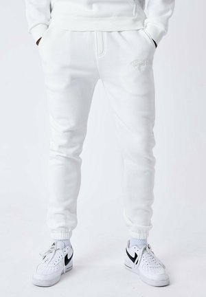 Witte sweatpants met elastische tailleband en boorden, zijzakken en subtiele borduursels. Gecombineerd met witte sneakers met zwarte accenten.