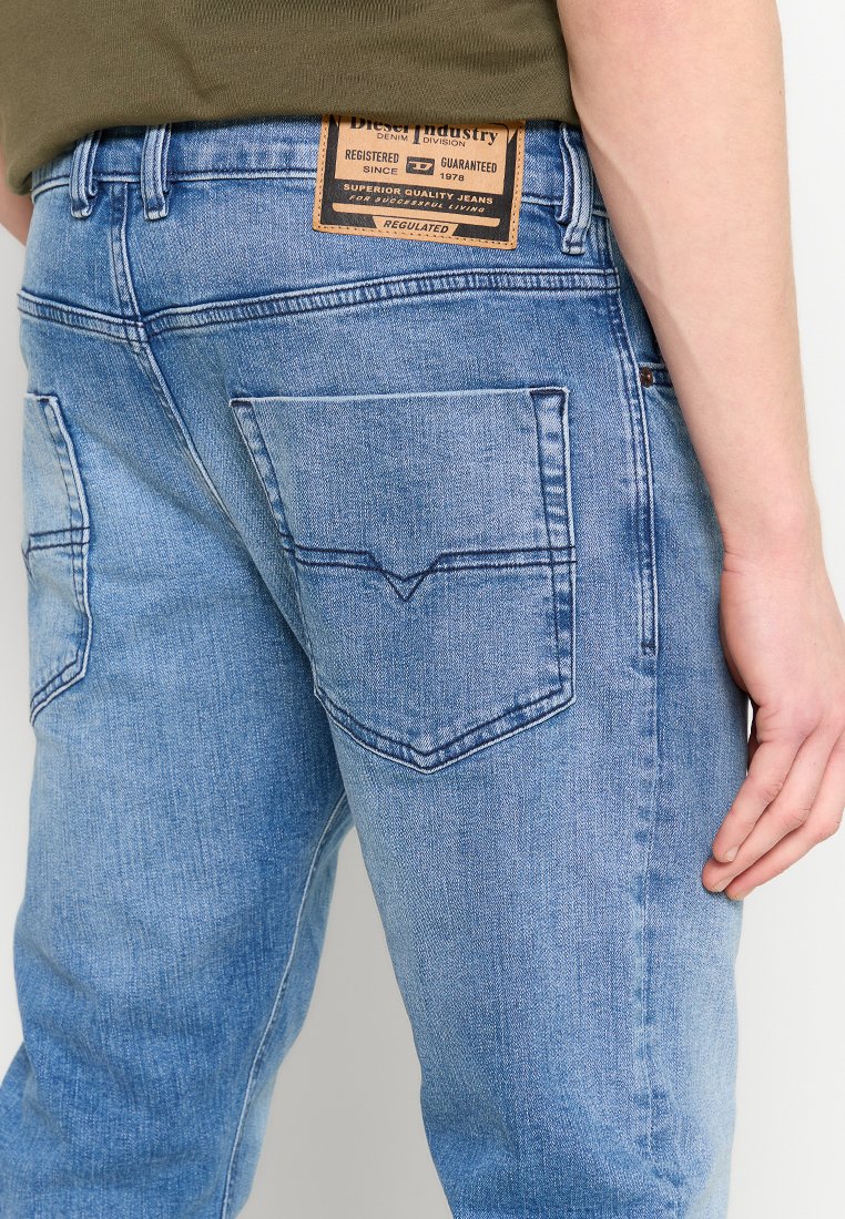 Jean en denim bleu clair avec une coupe décontractée, comportant deux poches arrière et une patch en cuir marqué au niveau de la taille. Texture lisse.