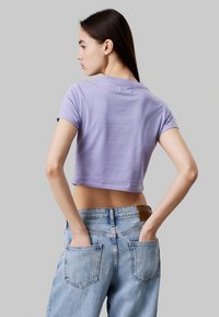 Camiseta corta de color lila con mangas cortas, textura suave, escote redondo, combinada con unos pantalones de mezclilla de tiro alto en azul claro que cuentan con bolsillos traseros.