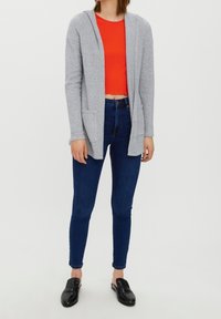 Grå huvtröja med fickor framtill, bärs över en röd kort topp, tillsammans med blå smala jeans och svarta slip-on skor.