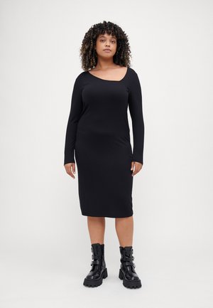 Black, long-sleeve ribbed dress with an asymmetrical neckline, fitted silhouette, knee-length, paired with chunky black buckled boots.