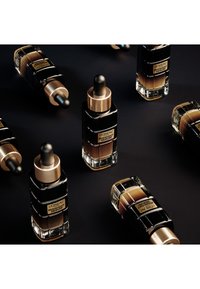 Bouteilles de sérum L'Oréal Midnight avec des accents noirs et dorés ; design en verre, bouchons à pipette, diverses teintes de sérum à l'intérieur, disposées artistiquement.