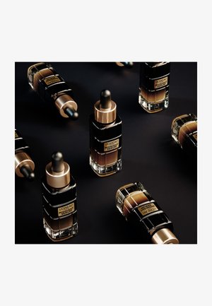 Bouteilles de sérum L'Oréal Midnight avec des accents noirs et dorés ; design en verre, bouchons à pipette, diverses teintes de sérum à l'intérieur, disposées artistiquement.