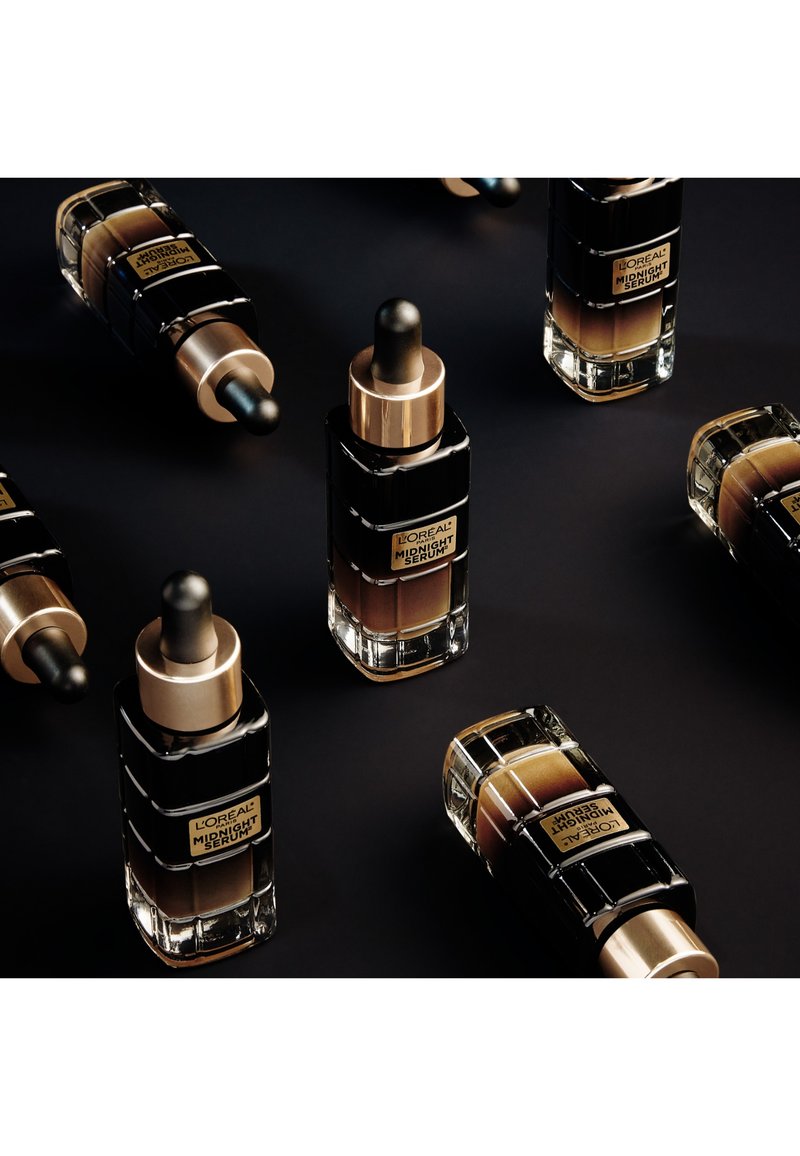 Bouteilles de sérum L'Oréal Midnight avec des accents noirs et dorés ; design en verre, bouchons à pipette, diverses teintes de sérum à l'intérieur, dispos ées artistiquement.