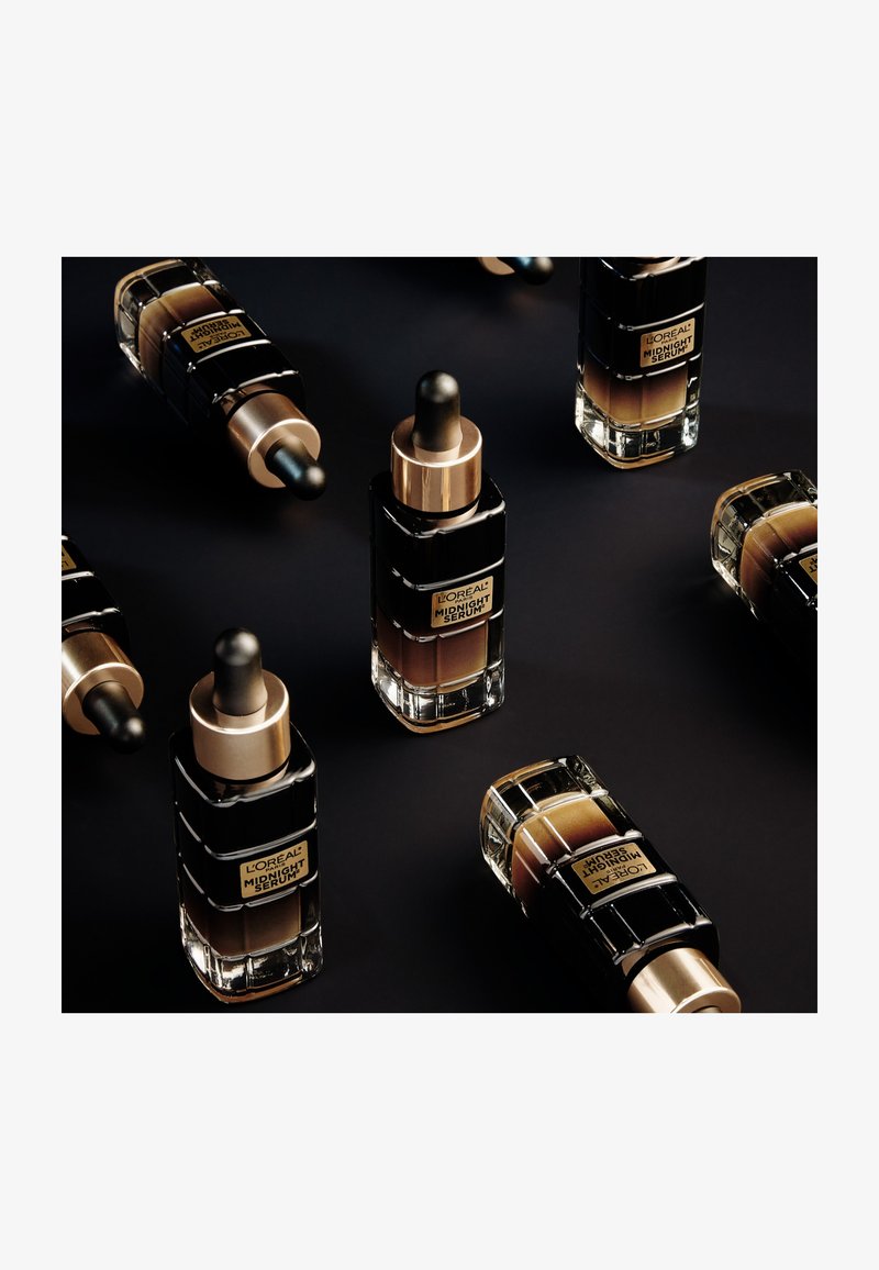 Bouteilles de sérum L'Oréal Midnight avec des accents noirs et dorés ; design en verre, bouchons à pipette, diverses teintes de sérum à l'intérieur, disposées artistiquement.