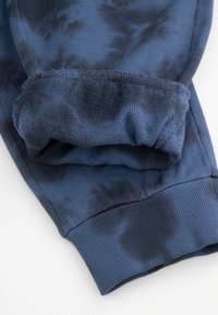 Granatowe dresy z mankietami przy kostkach i teksturowanym pasem, z wzorem tie-dye w różnych odcieniach ciemnego niebieskiego.
