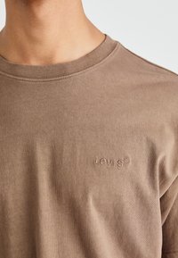 Rudas medvilninis marškinėliai su apvaliu kaklu, su reljefiniu Levi's logotipu išsiuvinėtu ant krūtinės. Minkšta, glotni medžiaga su laisvu siluetu.