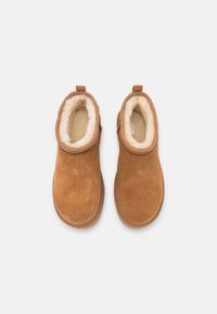 Paire de bottes d'hiver en daim beige avec doublure en fourrure blanche, vue de dessus sur un fond clair.