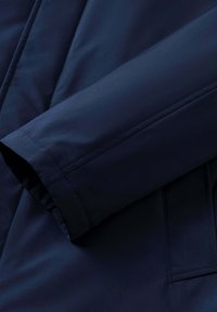 Marineblauwe gevoerde jas met details van de mouwen en zakken, zichtbaar stiksel en een gladde stoftextuur.