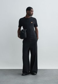 Must musta T-särk, millel on väike oranž looma tikand, koos laia musta pükste ja musta kotiga, millel on kokkuvõtva disain.