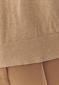 Brun, struktureret sweaterkant med en tætsiddende, glat bund. Begge lag er i nuancer af brun, hvilket fremhæver en subtil tonet kontrast.