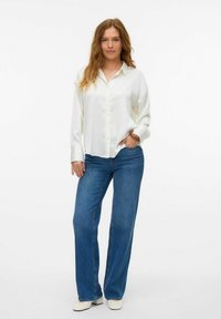Witte button-up blouse met lange mouwen, gecombineerd met wijdvallende blauwe jeans en lichtgekleurde schoenen. Soepele stof, relaxte pasvorm en klassiek ontwerp.