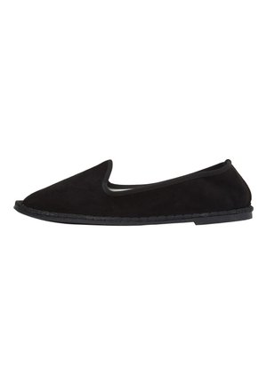 Scarpa slip-on in suede nero con punta arrotondata e bordo elastico. Presenta una suola piatta in gomma con cuciture dettagliate lungo il bordo.
