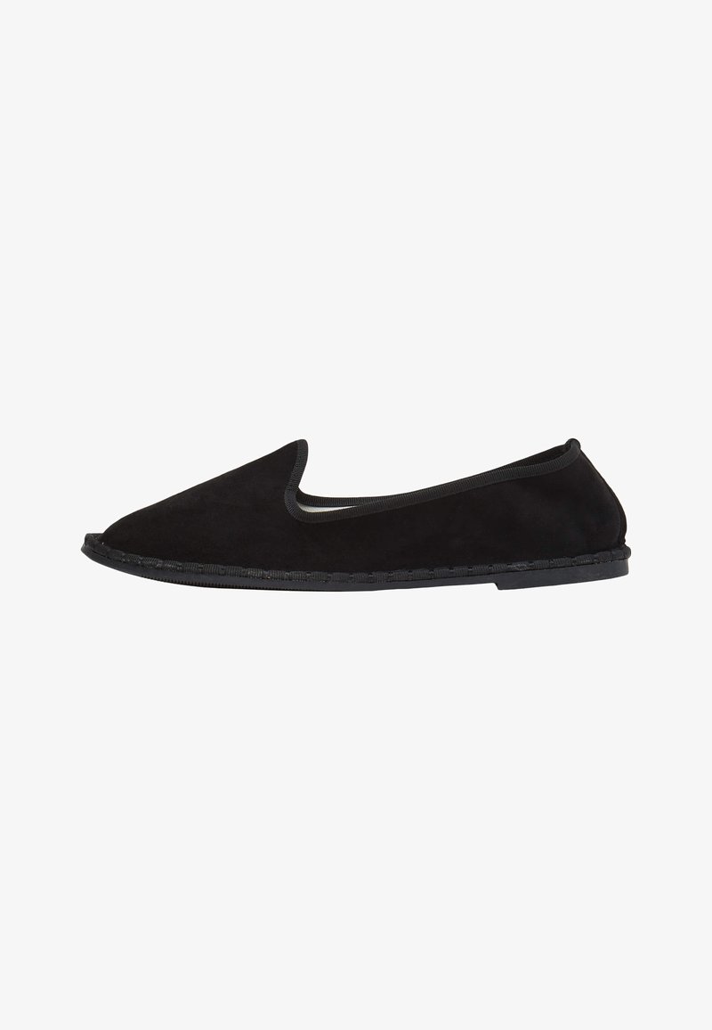 Scarpa slip-on in suede nero con punta arrotondata e bordo elastico. Presenta una suola piatta in gomma con cuciture dettagliate lungo il bordo.