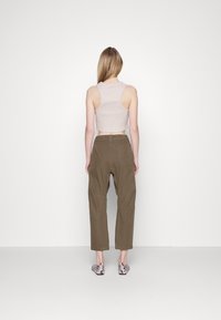 Ljusrosa ribbad kort topp parat med olivgröna vida byxor, med en bakfickadetalj. Skor med ormskinnstryck synliga.