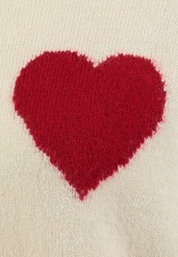 Maglione lavorato a maglia con un grande design a cuore rosso su uno sfondo crema chiaro, che mostra un motivo a maglia testurizzato.