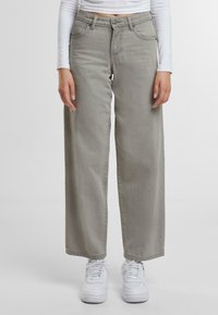 Vaqueros de pierna ancha gris claro con cintura alta, cinco bolsillos y detalles de costura sutiles; combinados con zapatillas blancas.
